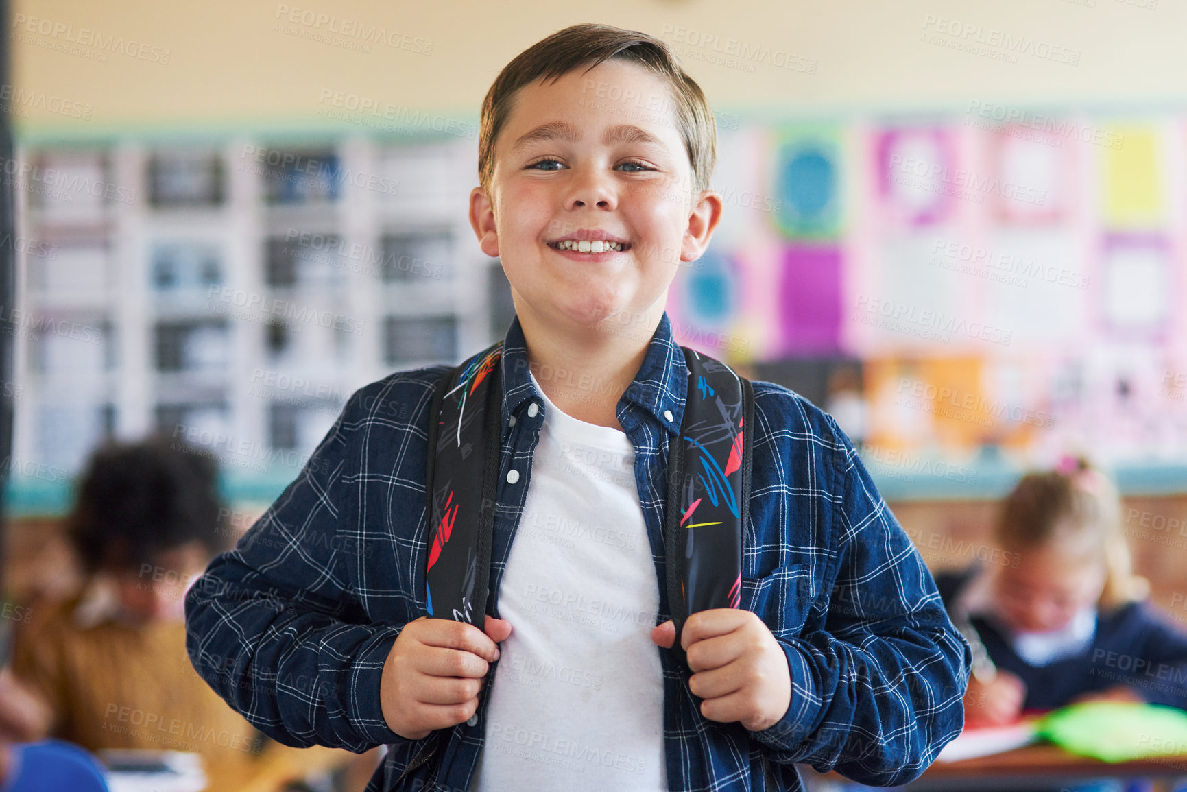 Buy stock photo Shot of a young boy standing in his classroom at school and holding his backpack