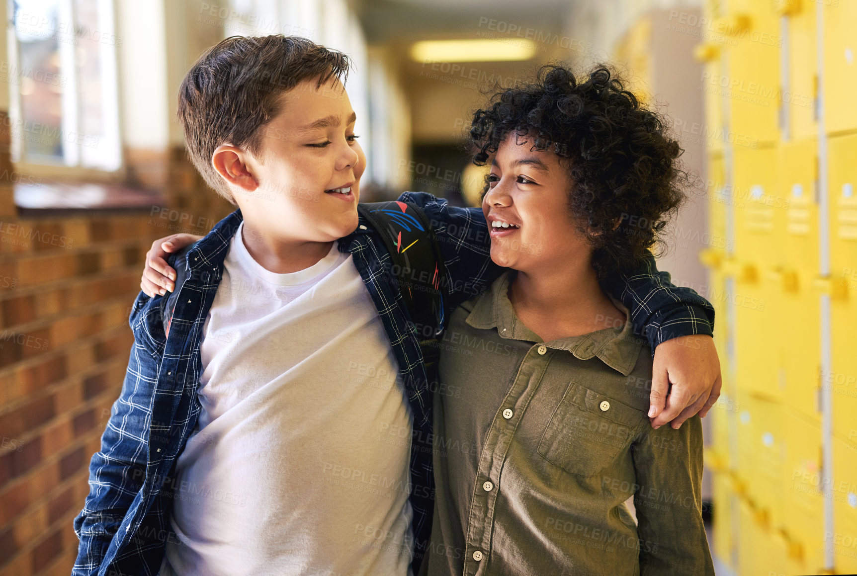 Buy stock photo Shot of two young boys standing in the hallway at school with their arms around each other