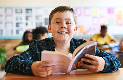 Buy stock photo Shot of a young boy sitting in his classroom at school and reading a book