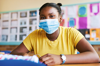 Buy stock photo Shot of a young girl sitting alone in her classroom at school and wearing a face mask