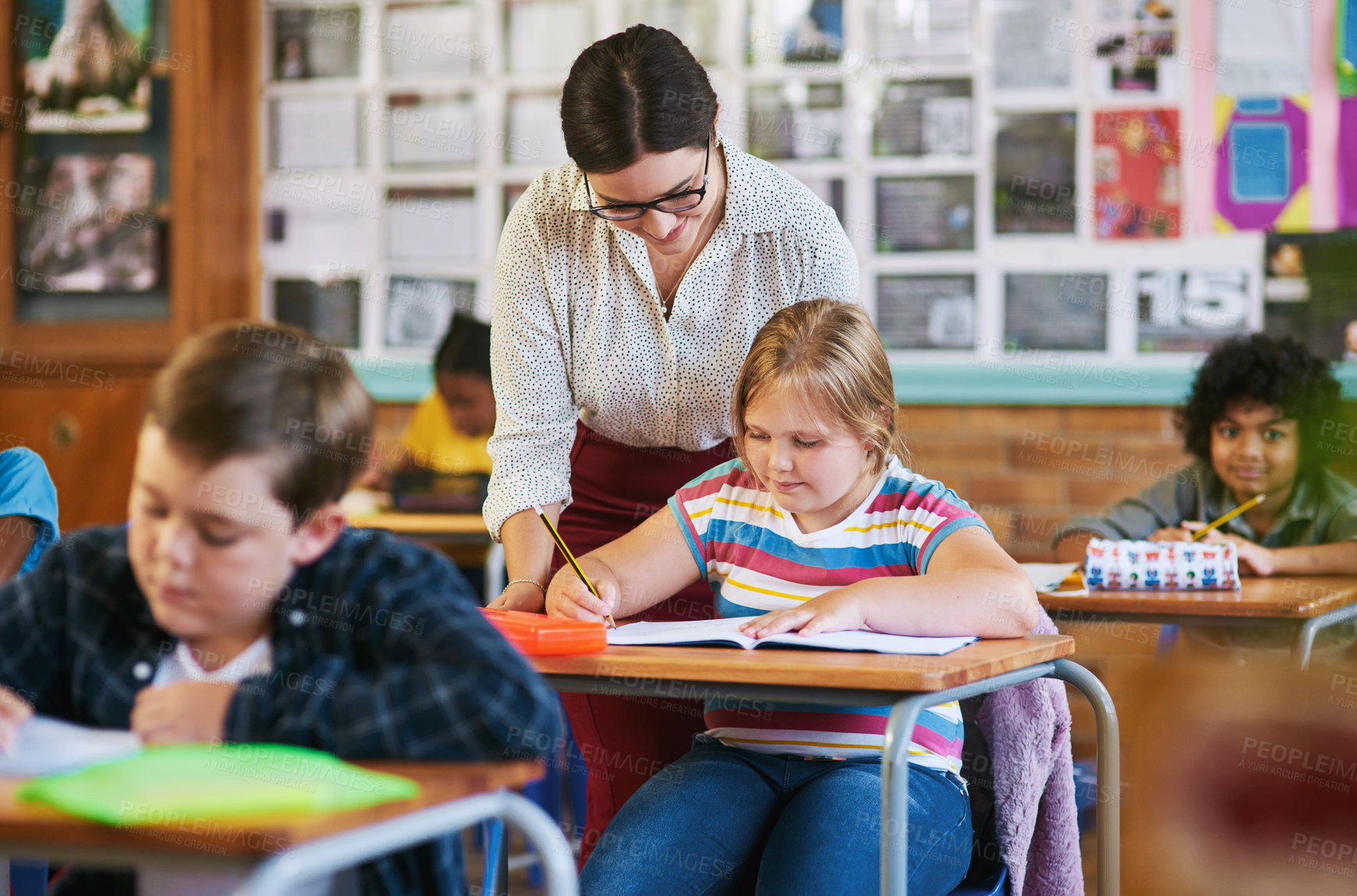 Buy stock photo Shot of an attractive young teacher helping a student in her classroom during a lesson