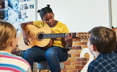 Buy stock photo Shot of a young girl sitting and playing the guitar for her classmates in the classroom at school