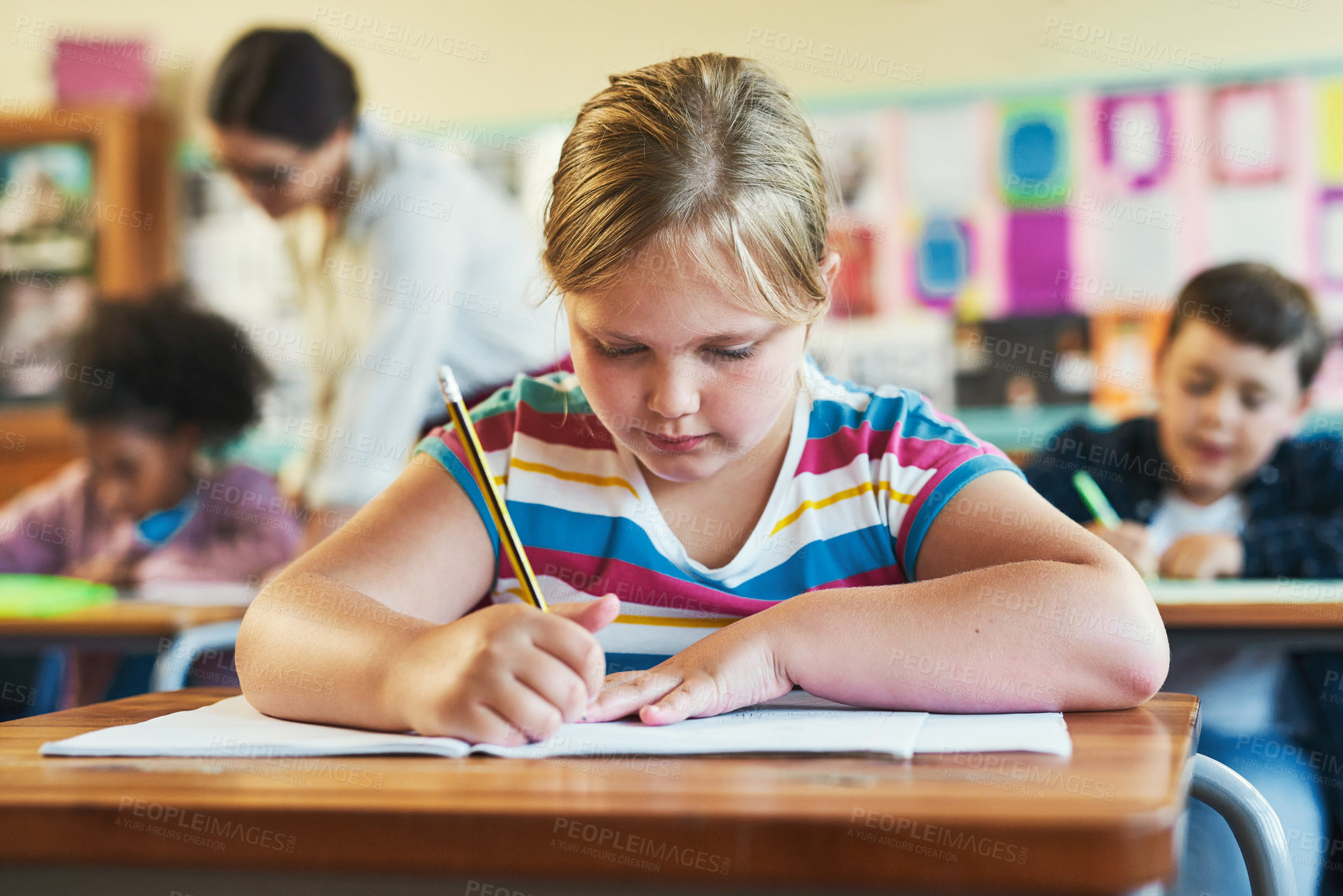 Buy stock photo Shot of a young girl sitting in her classroom at school and writing in her workbook