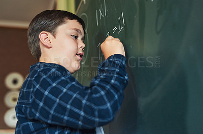 Buy stock photo Shot of a young boy standing alone and writing on the blackboard during a lesson in his classroom at school