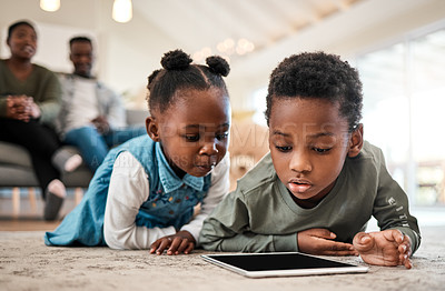 Buy stock photo Shot of an adorable little boy and girl using a digital tablet with their family in the background at home