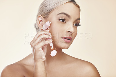 Buy stock photo Studio shot of a young woman using a jade derma roller on her face