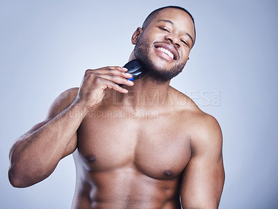 Buy stock photo Studio shot of a handsome young man shaving his facial hair with an electrical razor against a blue background