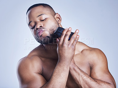 Buy stock photo Studio shot of a handsome young man shaving his facial hair with an electrical razor against a blue background