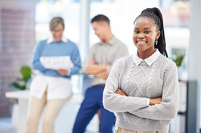 Buy stock photo Shot of an attractive young businesswoman standing in the office with her arms folded while her colleagues work behind her