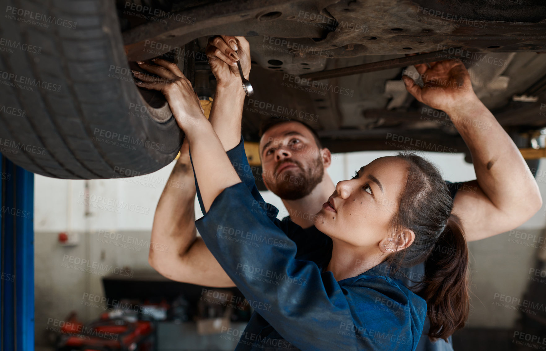 Buy stock photo Mechanic, garage and working on car with training, maintenance engineer and teamwork at workplace. Repair shop, trade and mentor with woman checking under wheel with technician and auto service