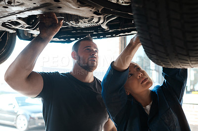 Buy stock photo Shot of two mechanics working together under a lifted car