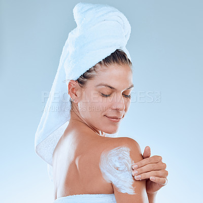 Buy stock photo Studio shot of a young woman applying moisturiser to her body after a shower against a blue background