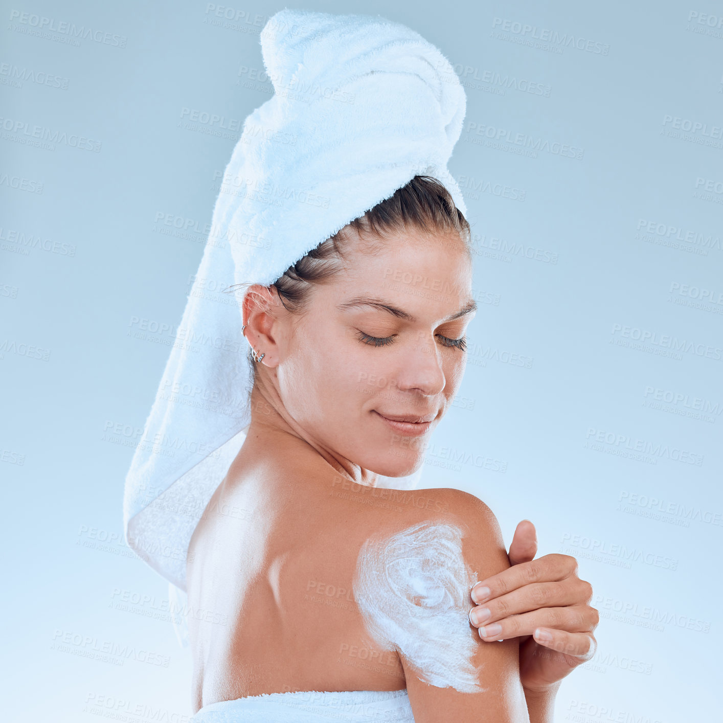 Buy stock photo Studio shot of a young woman applying moisturiser to her body after a shower against a blue background