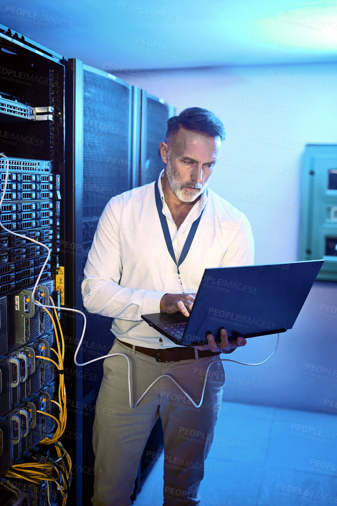 Buy stock photo Shot of a mature man using a laptop while working in a server room