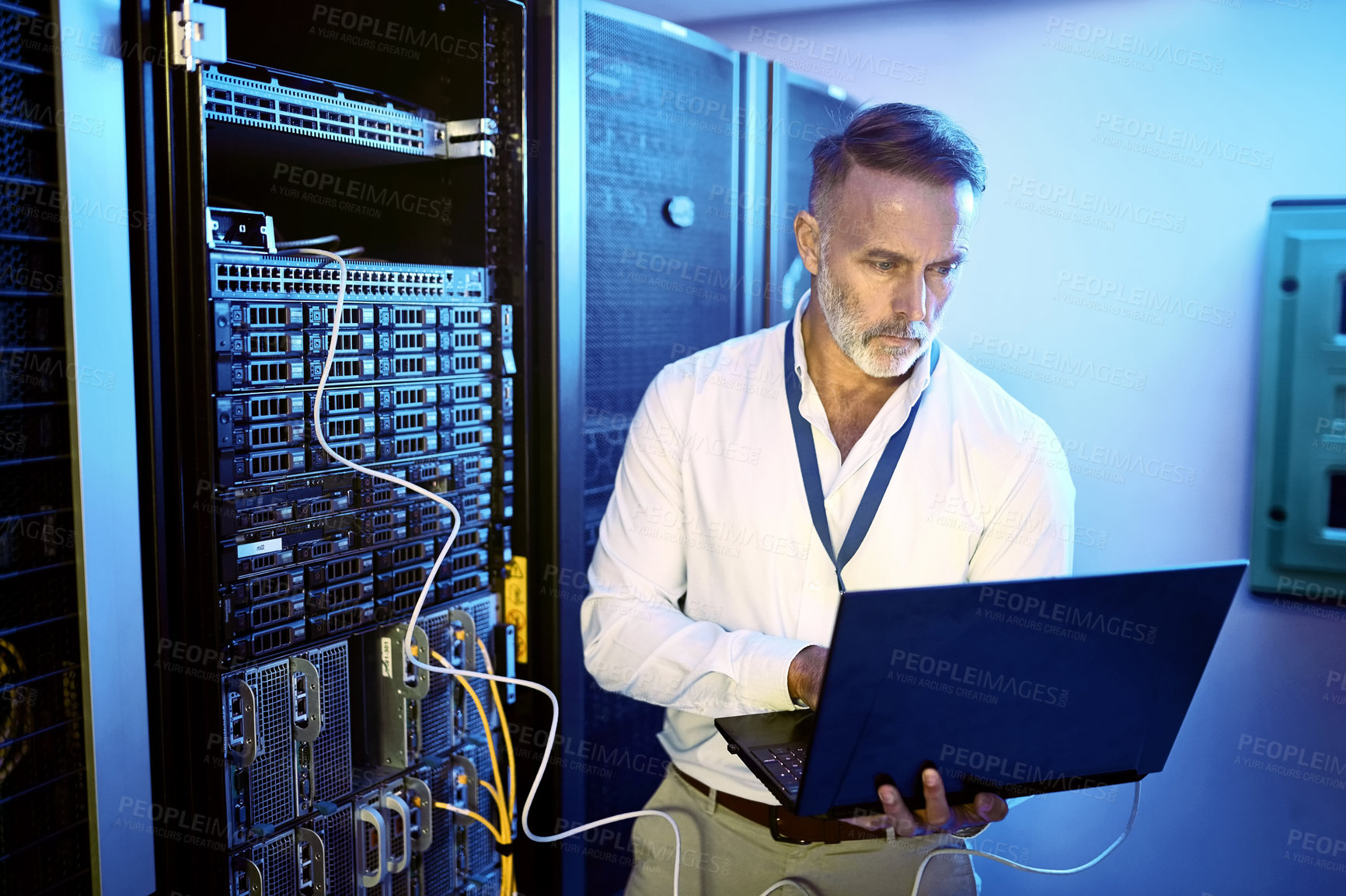 Buy stock photo Shot of a mature man using a laptop while working in a server room