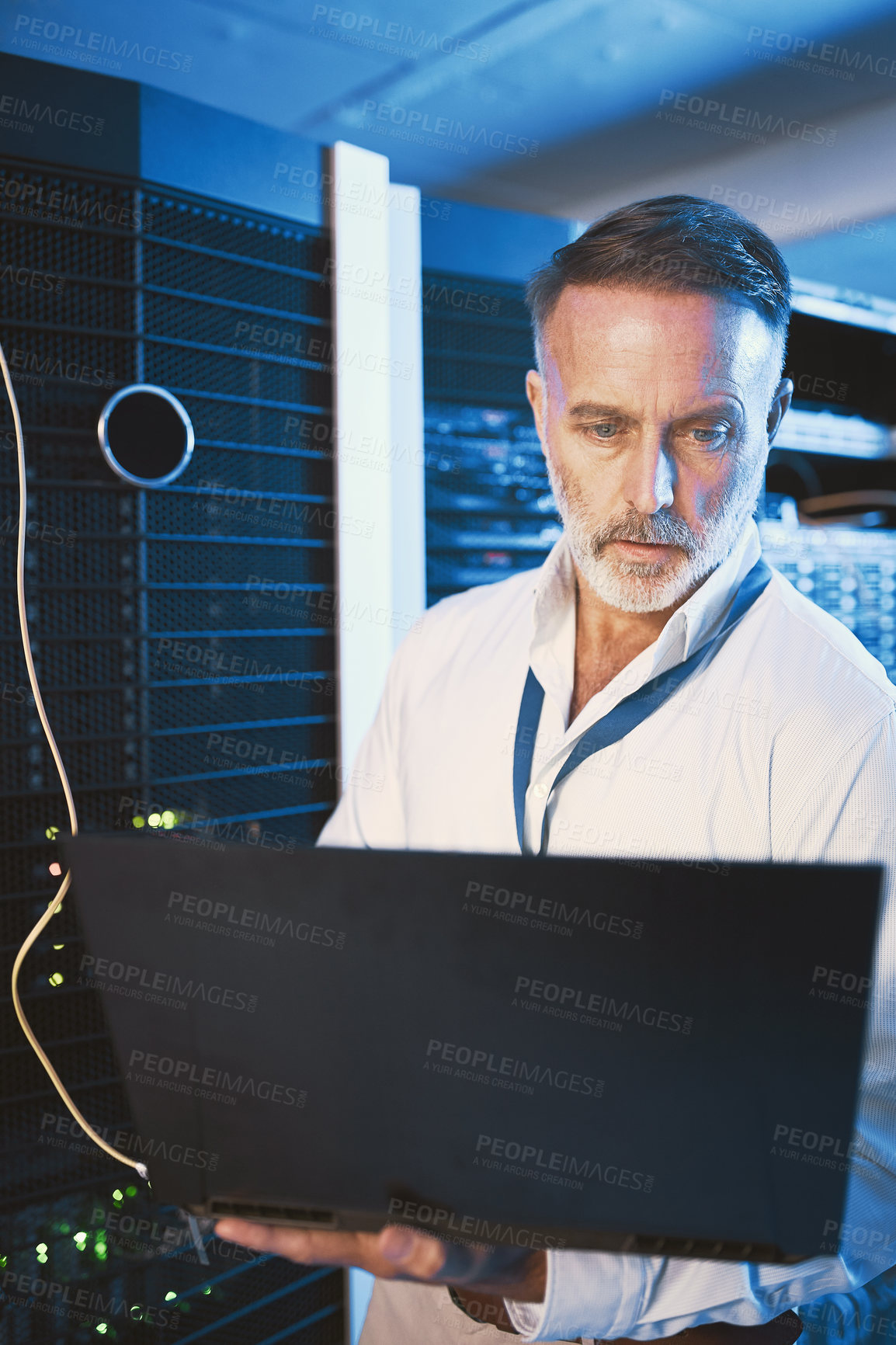 Buy stock photo Shot of a mature man using a laptop while working in a server room