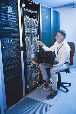 Buy stock photo Shot of a mature man using a laptop while working in a server room