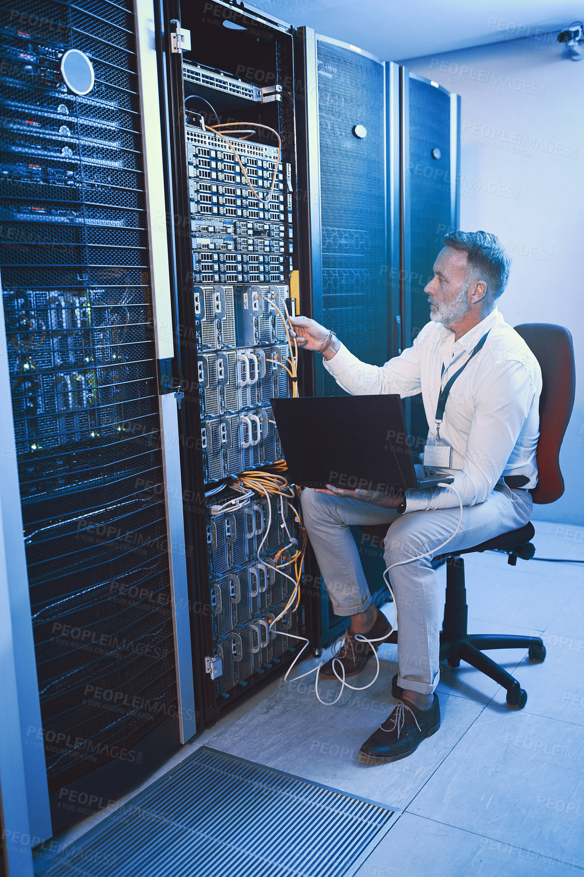 Buy stock photo Shot of a mature man using a laptop while working in a server room