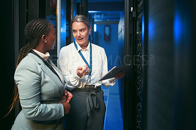 Buy stock photo Shot of two young IT specialists standing in the server room and having a discussion while using a digital tablet