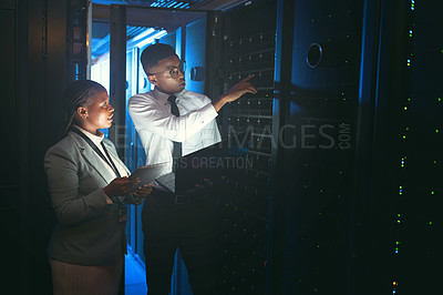 Buy stock photo Shot of two young IT specialists standing in the server room and having a discussion while using a technology