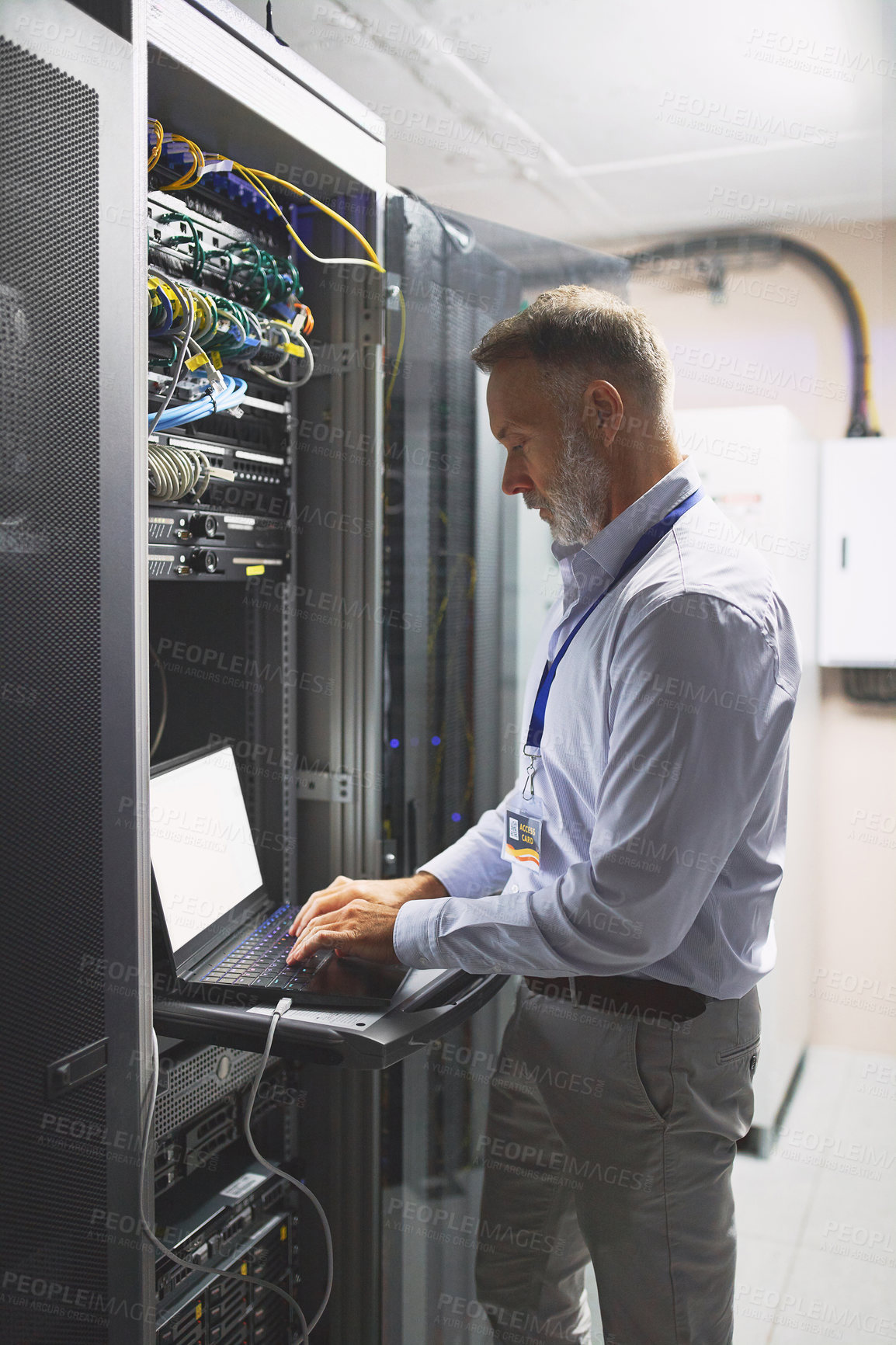 Buy stock photo Shot of a mature man using a laptop while working in a server room