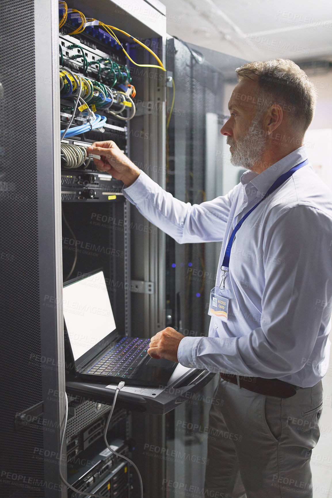 Buy stock photo Shot of a mature man using a laptop while working in a server room