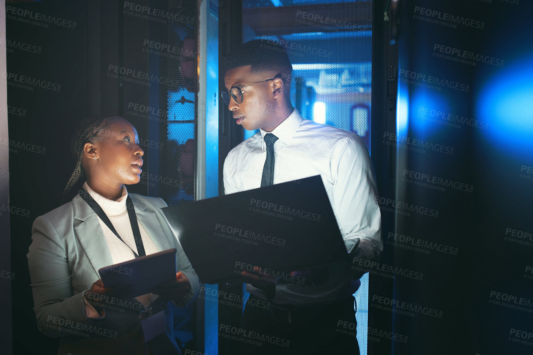 Buy stock photo Shot of two young IT specialists standing in the server room and having a discussion while using a technology