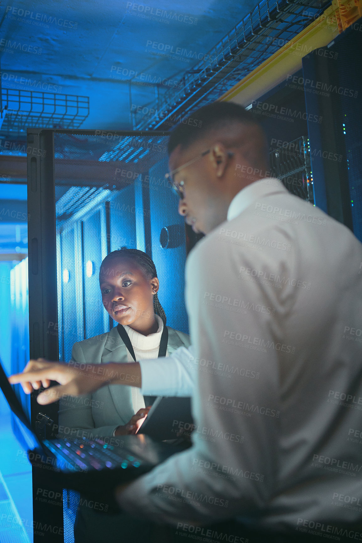 Buy stock photo Shot of two young IT specialists standing in the server room and having a discussion while using a technology