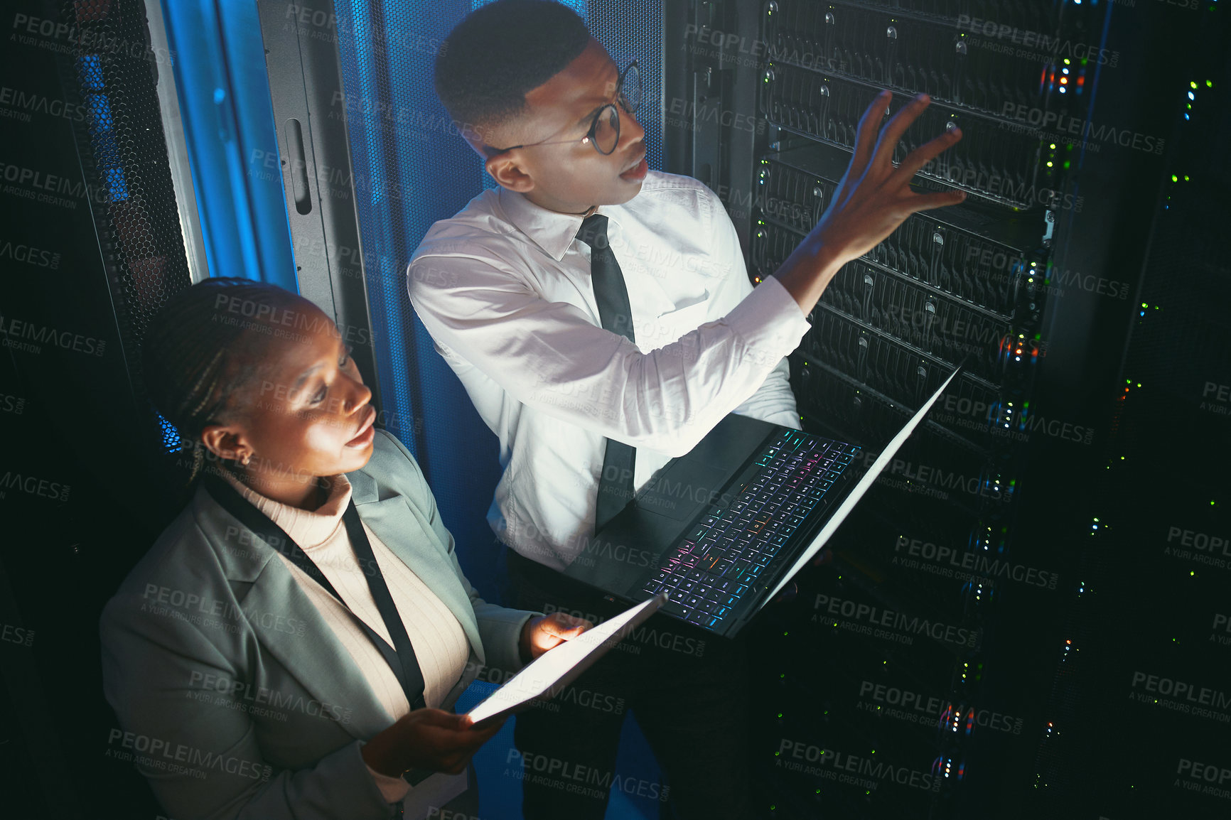 Buy stock photo Shot of two young IT specialists standing in the server room and having a discussion while using a technology