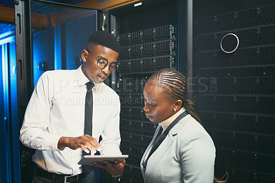 Buy stock photo Shot of two young IT specialists standing in the server room and having a discussion while using a digital tablet