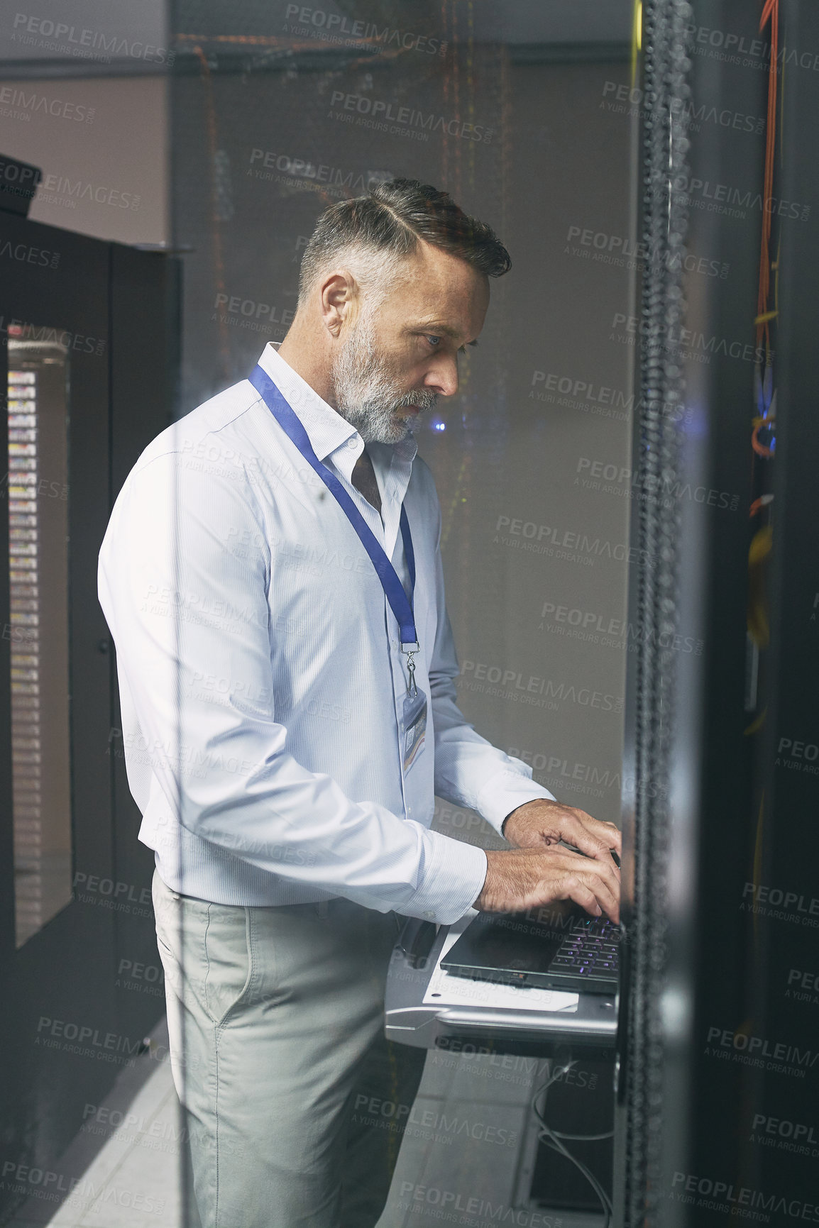 Buy stock photo Shot of a mature man using a laptop while working in a server room