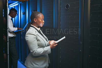 Buy stock photo Shot of two young IT specialists standing together in the server room and using technology