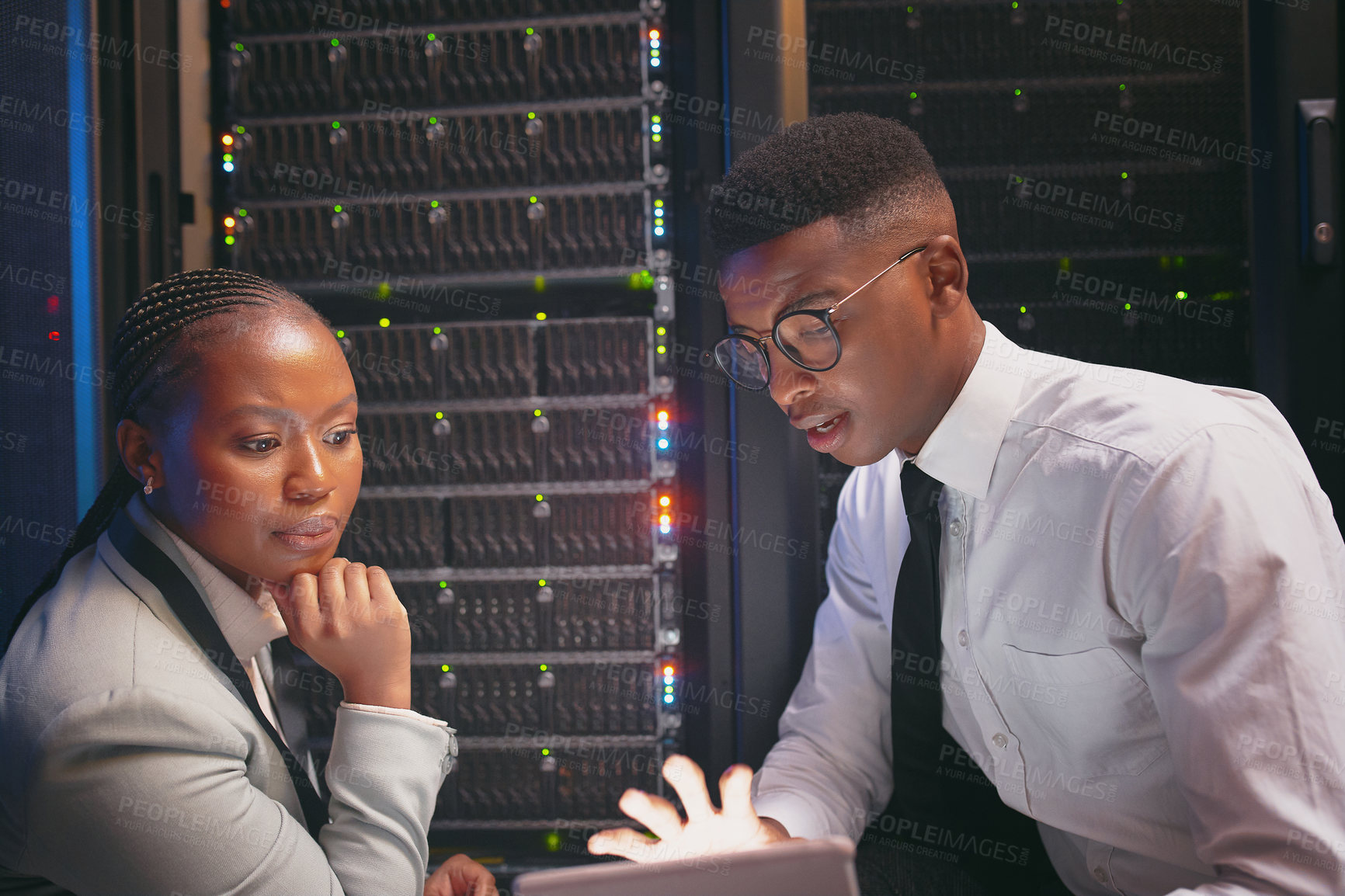 Buy stock photo Shot of two young IT specialists crouched down in the server room together and using a digital tablet