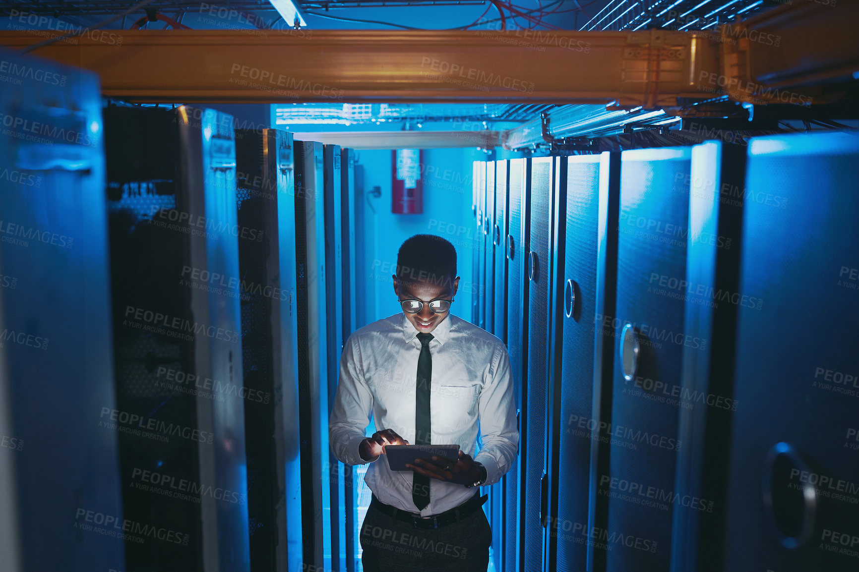 Buy stock photo Shot of a young IT specialist standing alone in the server room and using a digital tablet