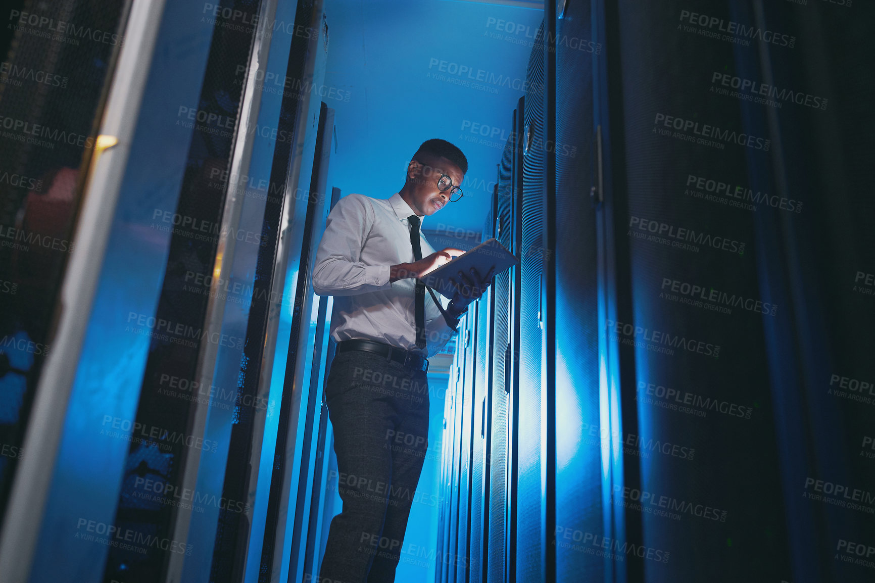 Buy stock photo Shot of a young IT specialist standing alone in the server room and using a digital tablet