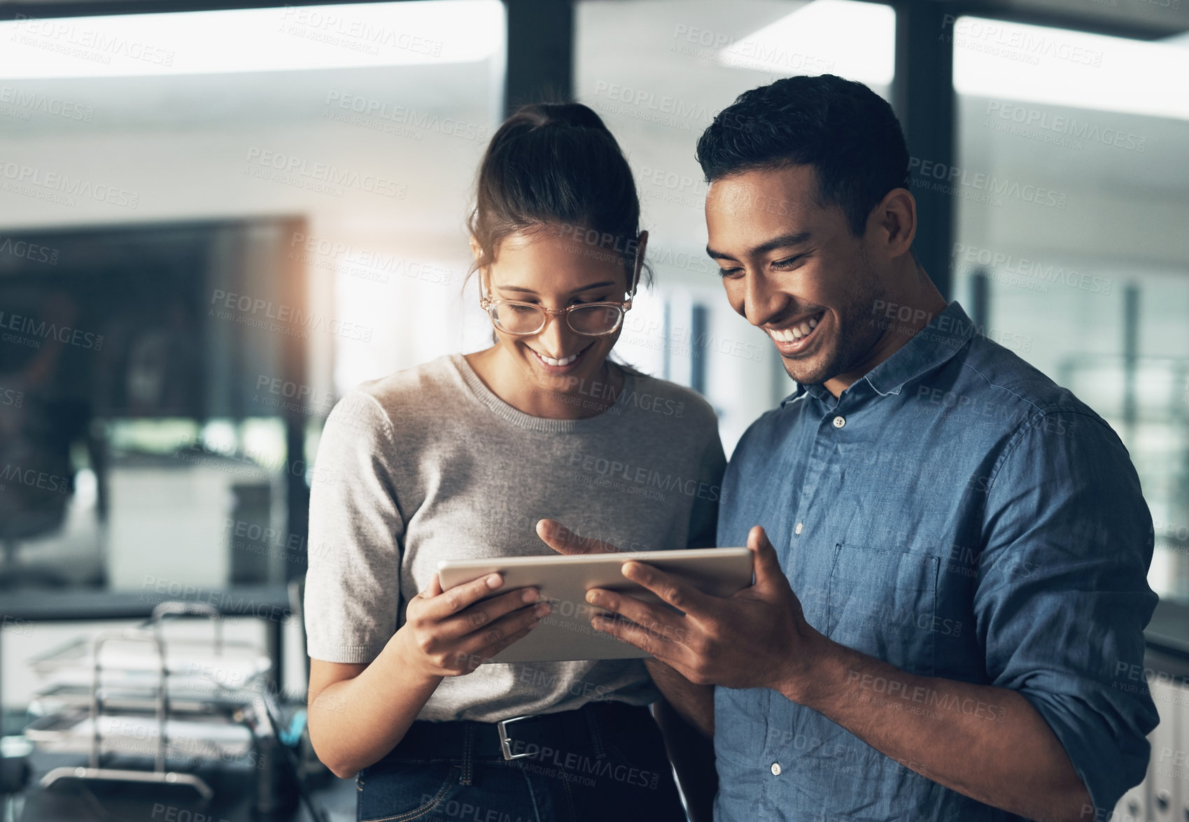 Buy stock photo Shot of two young workers using a digital tablet in a modern office