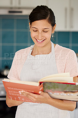 Buy stock photo Shot of a young woman reading a cook book