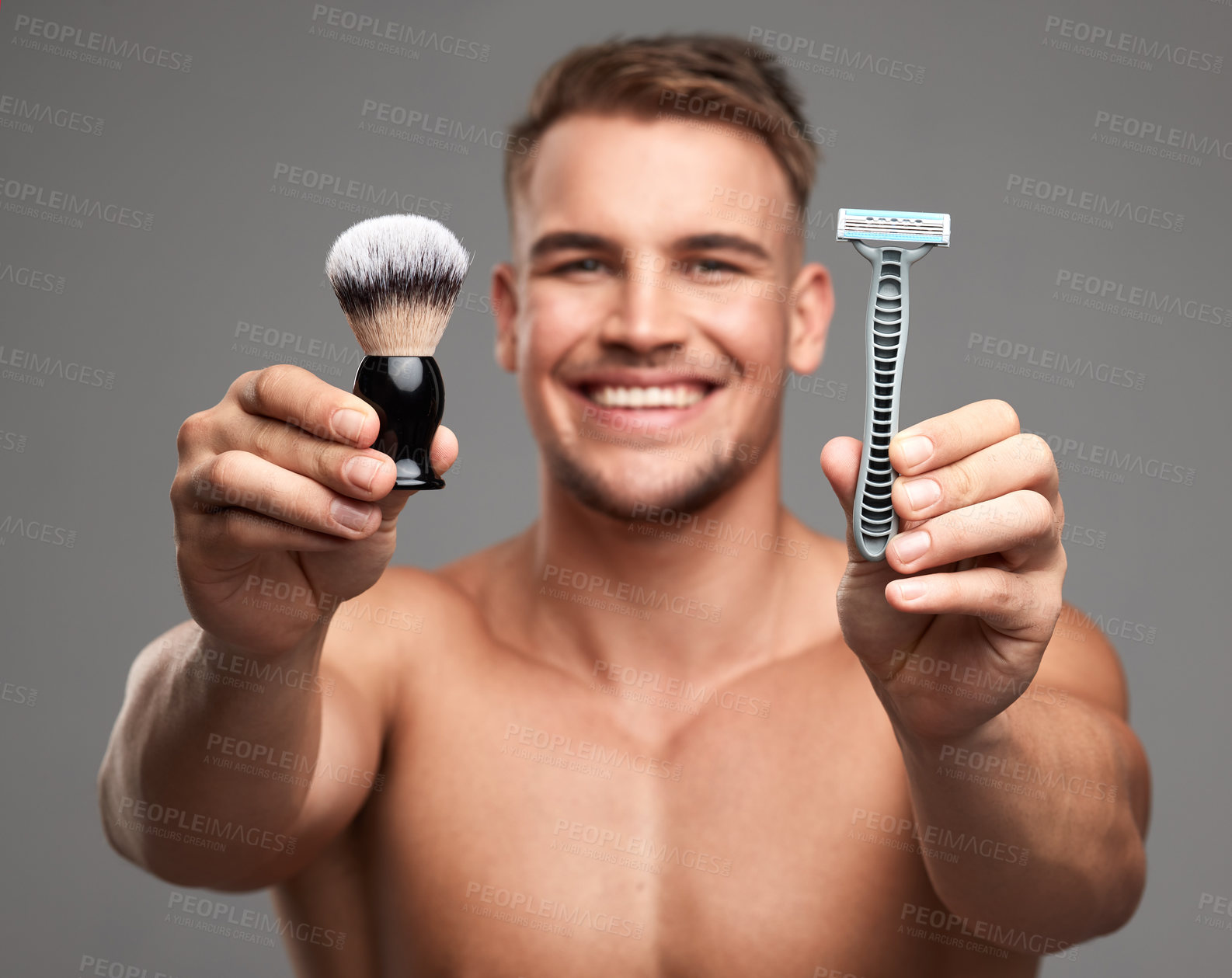 Buy stock photo Studio shot of a handsome young man holding a razor and brush against a grey background