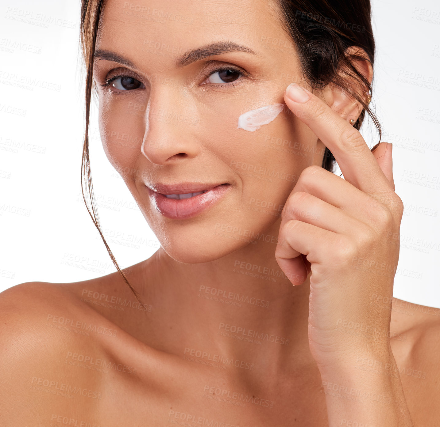 Buy stock photo Shot of an attractive young woman applying moisturiser to her face in the studio