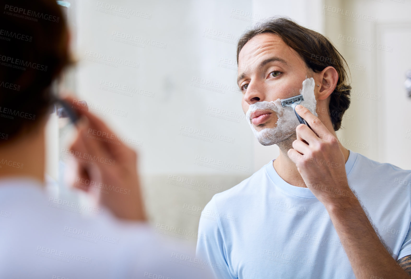 Buy stock photo Shot of a young man shaving his face in the morning