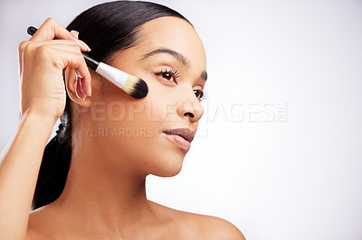 Buy stock photo Studio shot of a beautiful young woman applying makeup to her face with a brush against a white background