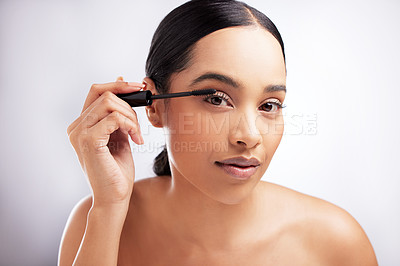 Buy stock photo Studio portrait of a beautiful young woman applying mascara against a white background