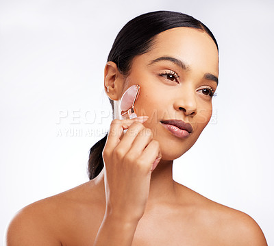Buy stock photo Studio shot of a beautiful young woman using a jade roller on her face against a white background