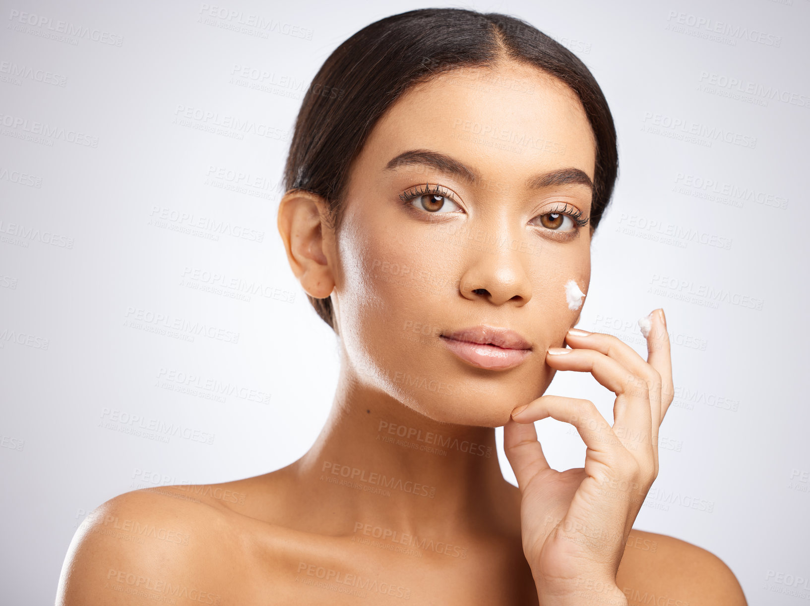 Buy stock photo Studio shot of an attractive young woman applying moisturiser to her face against a grey background