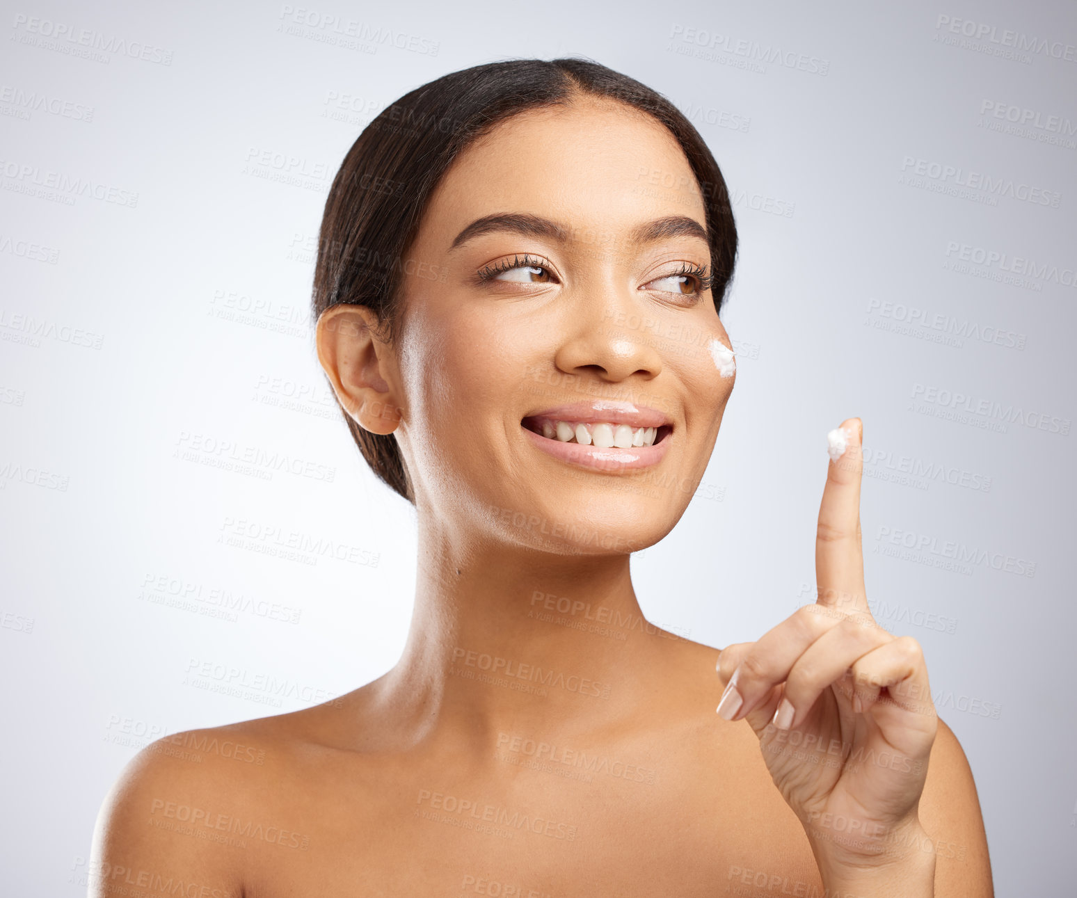 Buy stock photo Studio shot of an attractive young woman applying moisturiser to her face against a grey background