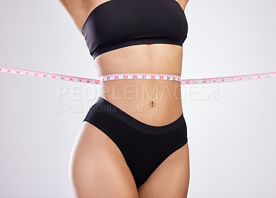 Buy stock photo Studio shot of an unrecognisable woman posing with a tape measure around her waist against a white background