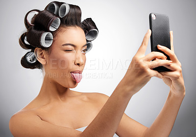 Buy stock photo Studio shot of an attractive young woman taking selfies with curlers in her hair against a grey background