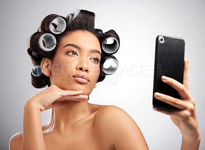 Buy stock photo Studio shot of an attractive young woman taking selfies with curlers in her hair against a grey background