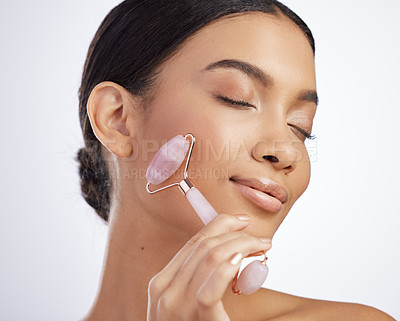 Buy stock photo Studio shot of an attractive young woman using a jade roller on her face against a grey background