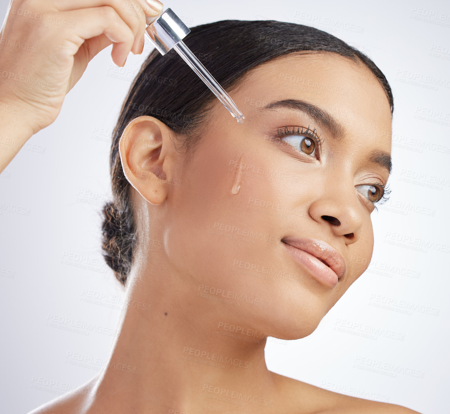 Buy stock photo Studio shot of an attractive young woman using a serum on her face against a grey background